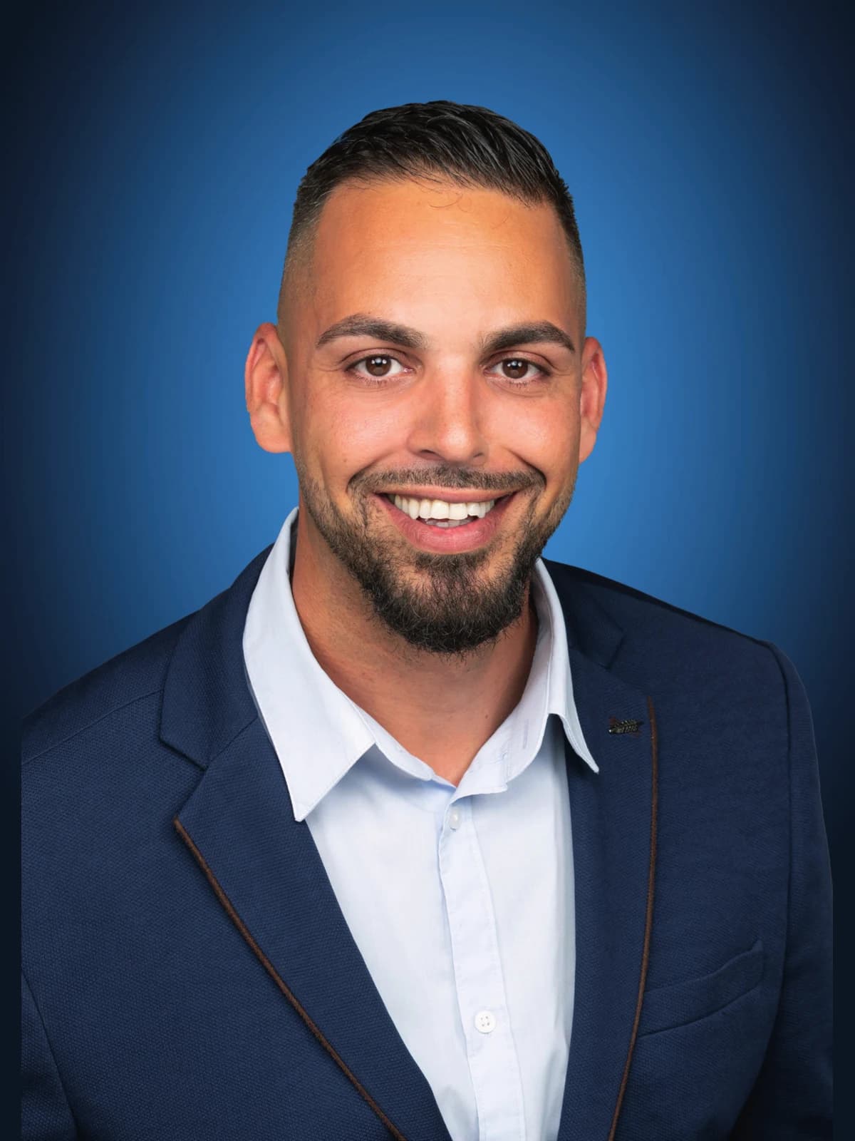 Mike Zaroual, en veste bleue, souriant devant un fond bleu